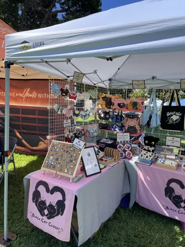 An angled view of the booth from the aisle, showing the pin board, illustrated bags, and sticker display
