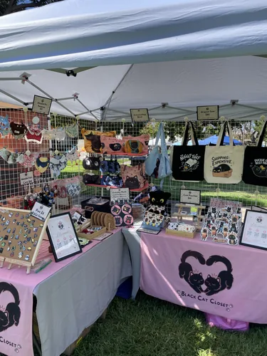 Inside the tent — pet bandanas strung across the grid wall, wool-felt cats, cork coasters, and the enamel pin board on its easel