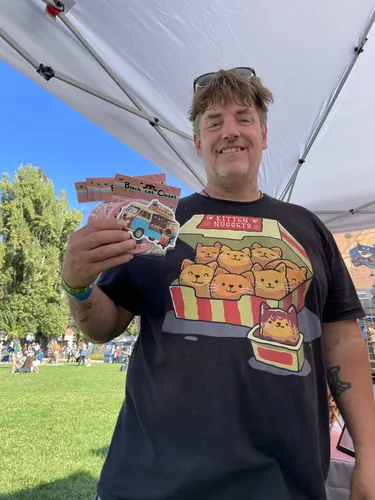 A customer in a kitten nuggets t-shirt holding a stack of sticker packs including the Black Cat Boba Tea van