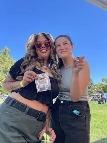 Two friends at the booth with a boba cat die-cut sticker and a small black cat enamel pin