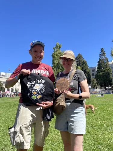 Two customers on the lawn holding up a Nugget Thief tote bag and a wooden cat coaster