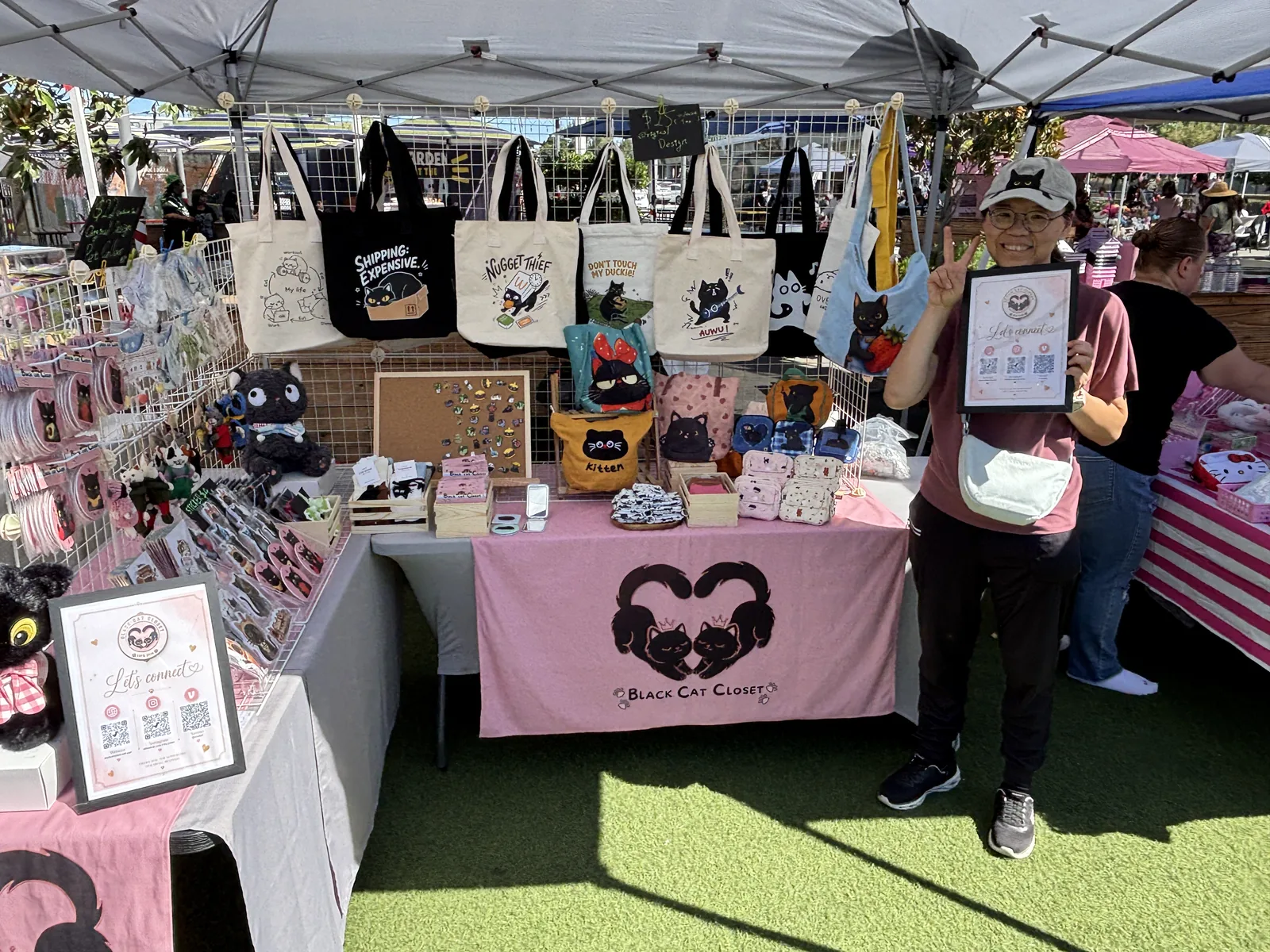 Holding our "Let's connect" sign at the Nyangi Studio USA booth, with cat tote bags on display behind