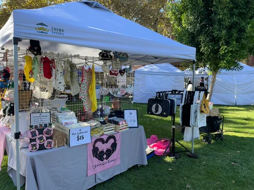 An angled view of the booth from the aisle, with pet bandanas strung across the grid wall, coasters and the Pet Collection sign on the table, and the tote rack outside the tent