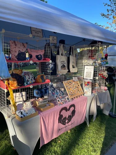 The front of our booth in the afternoon sun with the Nugget Thief, Shipping: Expensive, and Duckie Is My Best Friend tote bags hanging on the grid wall