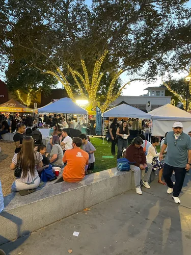 Food vendor tents along the plaza with string-lit trees overhead and a line of people waiting