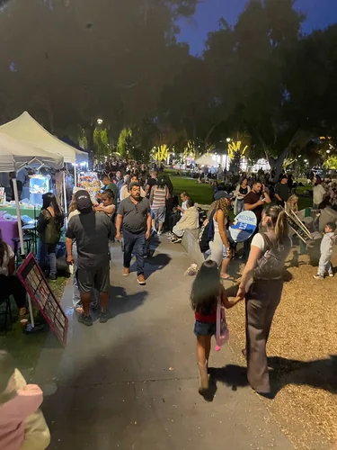 The plaza walkway packed with people after dark, vendor tents on one side and lit-up trees down the path