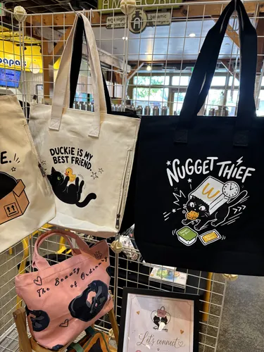 Duckie Is My Best Friend, Nugget Thief, and Beauty of Ordinary cat tote bags on display