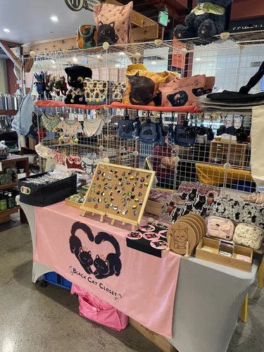 An angled view of the full booth showing the illustrated tote bags, bandana line, and pin display