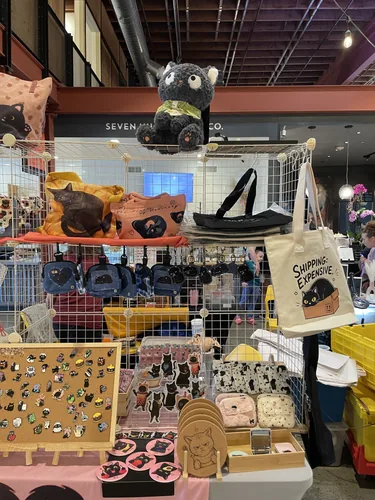 Enamel pin board, Black Cat Boba Tea die-cut stickers, quilted coin purses, and cork cat coasters on the table