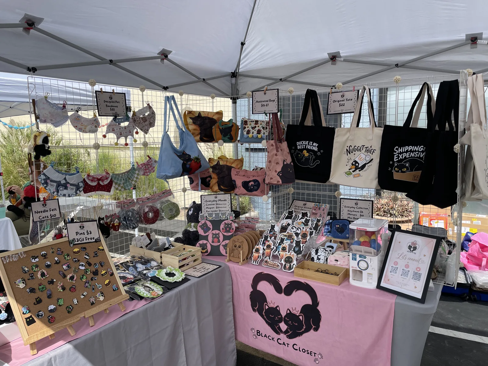 The Nyangi Studio USA booth at Head West Marketplace, with cat tote bags, pet bandanas, enamel pins, and the pink Black Cat Closet table banner