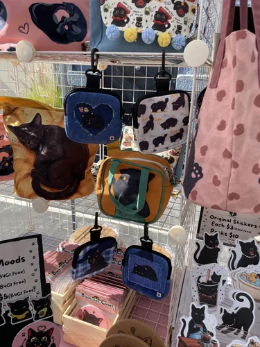 Denim and printed mini crossbody pouches clipped to the grid wall beside black cat sticker sheets
