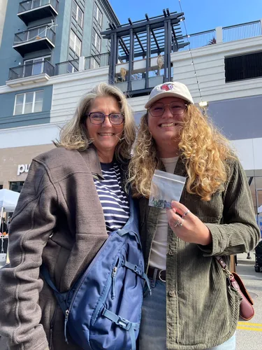 Two customers smiling together, one holding up a packet of enamel pins from our booth