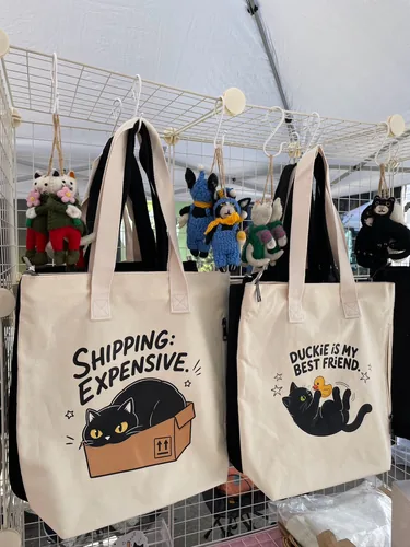The Shipping: Expensive and Duckie Is My Best Friend totes in natural canvas, with crocheted and wool-felt cat charms hanging above
