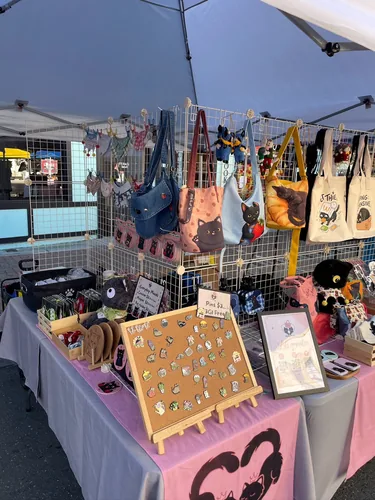 An angled view of the table with the enamel pin board on its easel, shoulder bags and tote bags on the grid wall, and our Let's Connect sign