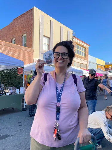 A customer holding up a black cat boba sticker on a bright blue-sky morning on Main Street