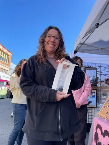 A customer smiling with her purchase in a window-front paper bag