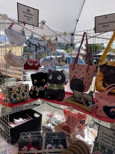 Pet bandanas clipped along the grid wall above two black cat plushies, a patterned crossbody bag, and a tray of scrunchies