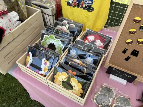 Wooden crates of handmade cat collar accessories with burger pins on a corkboard