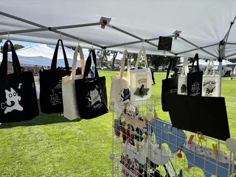 Black cat tote bags hanging along the inside of the booth tent